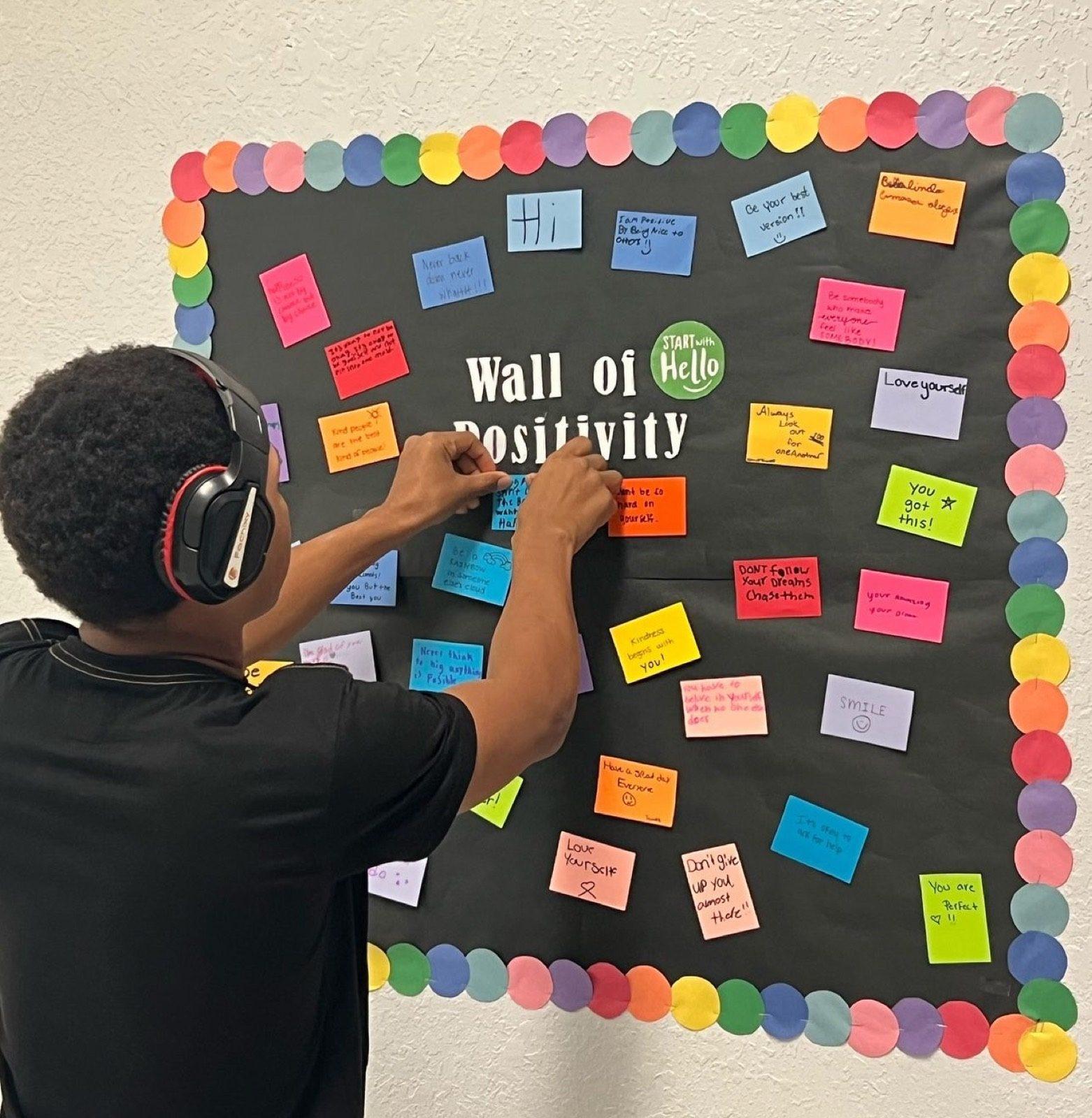 A student adding a note to a classroom wall of positivity